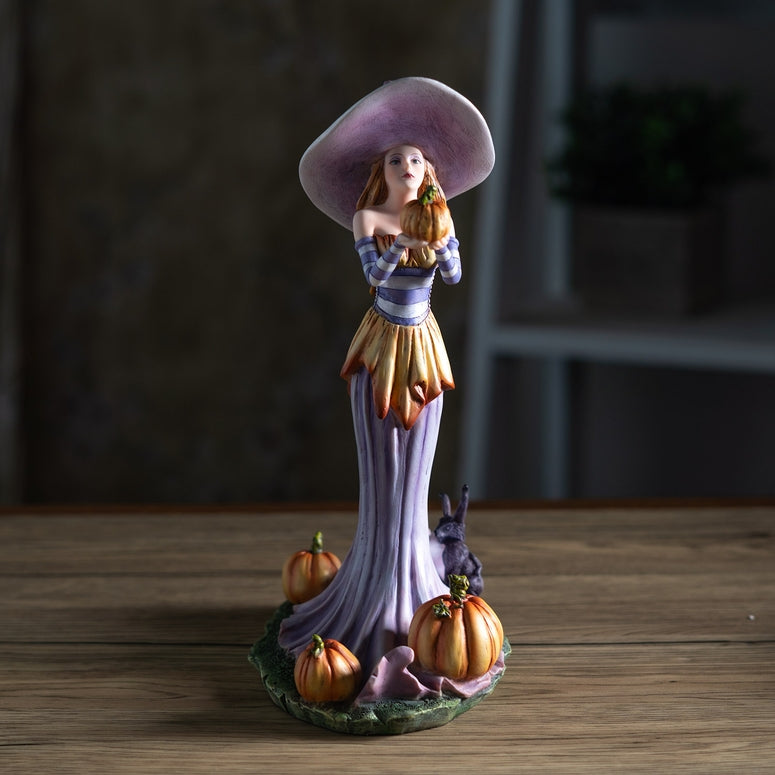 Decorative figurine of a woman with a large hat and pumpkins on a wooden surface
