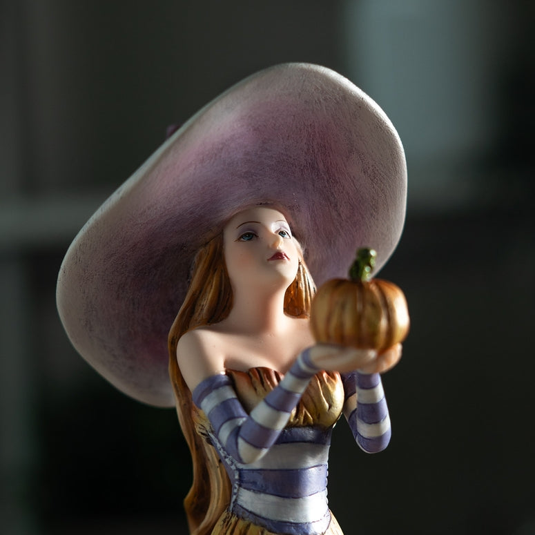 Figurine of a woman with a large hat holding a small pumpkin against a dark background