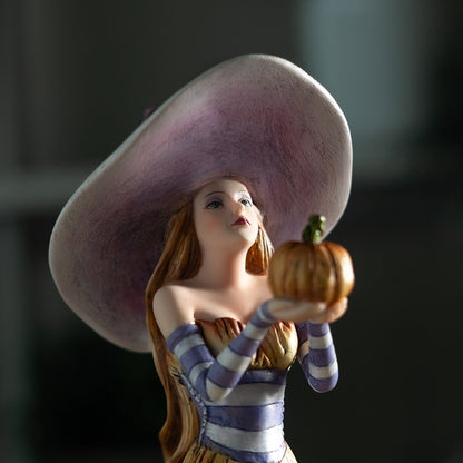 Figurine of a woman with a large hat holding a small pumpkin against a dark background