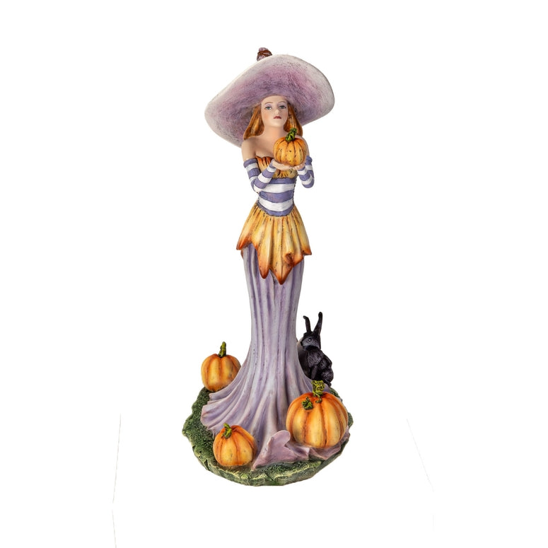 A painted resin figurine of a woman in a large lavender hat and striped top holding a pumpkin, with a long flowing lavender skirt, orange pumpkins around her, and a small black rabbit on a decorative base.