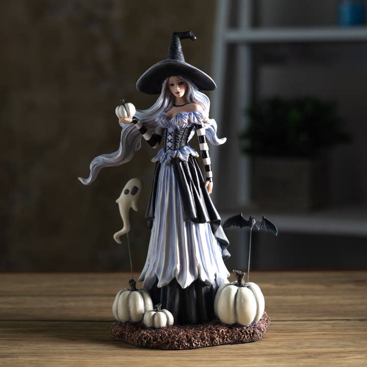 Halloween-themed figurine of a witch with pumpkins and a ghost on a wooden surface.