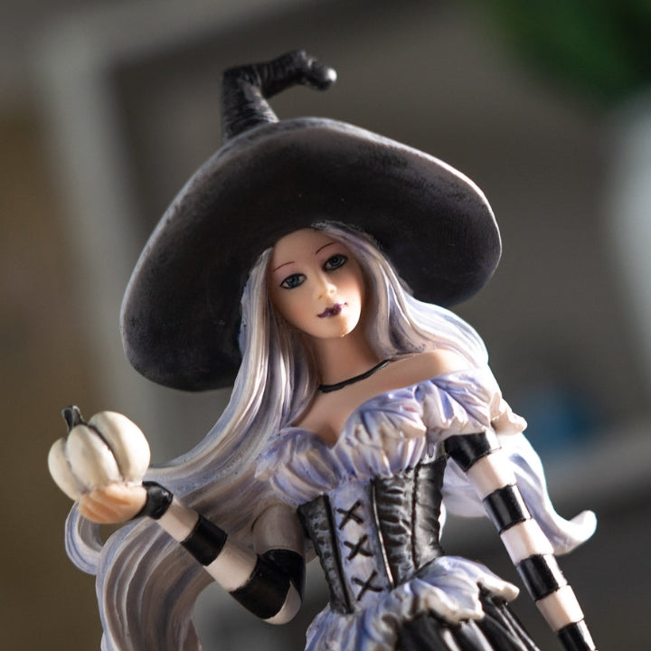 Toy figure of a witch with a black hat and white outfit holding an apple, against a blurred background.