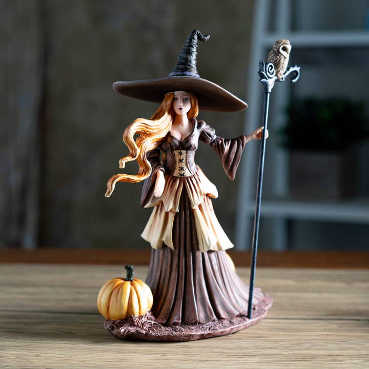 Witch figurine with a pumpkin on a wooden surface