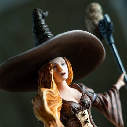 Statue of a witch with a large hat and broomstick against a dark background