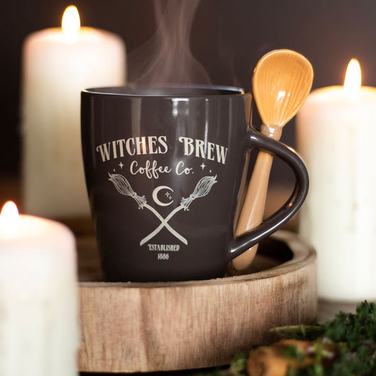 Black mug with 'Witches Brew Coffee Co.' text and design, surrounded by candles and a wooden spoon.