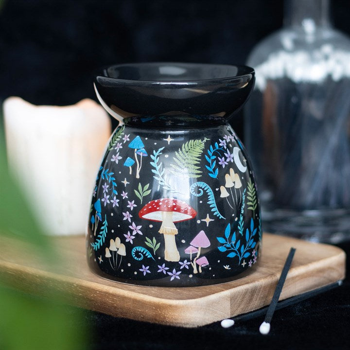 A black ceramic oil burner with a glossy finish, decorated with a whimsical woodland pattern of red and pink mushrooms, green ferns, blue flowers, and stars.