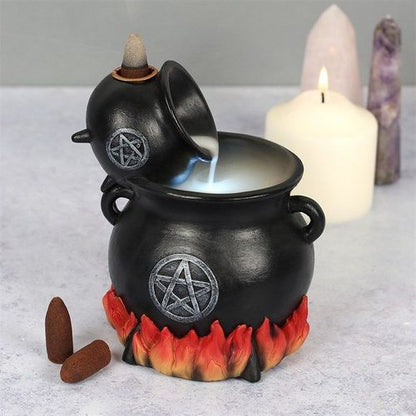 A black cauldron-shaped backflow incense holder with a silver pentagram design, featuring a small cone of incense burning on top, creating smoke. The holder is adorned with a distressed silver pentagram and there are flame accents around the base.