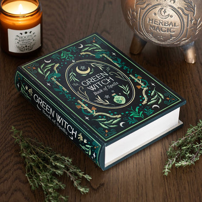 Decorative book titled 'Green Witch Book of Spells' on a wooden surface with herbs and a candle.