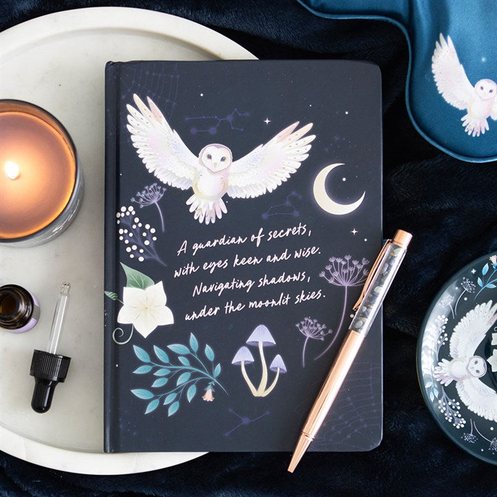 Dark notebook with owl illustration and text, surrounded by a candle, pen, and decorative items.
