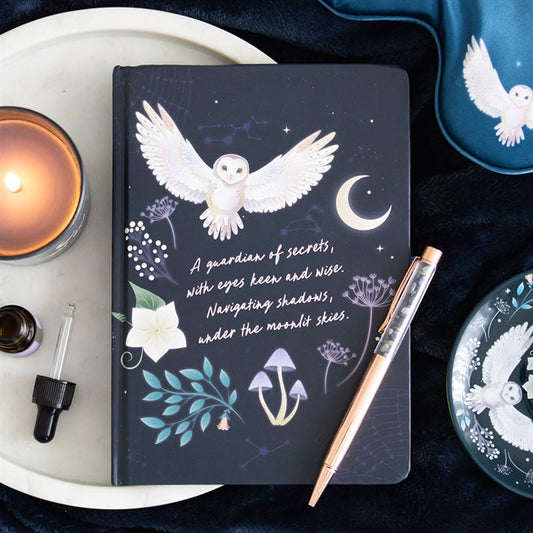 Dark notebook with owl illustration and text, surrounded by a candle, pen, and decorative items.