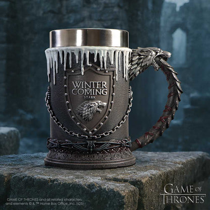 Decorative mug with 'Winter is Coming' and Stark logo on a stone surface with a dark, textured background.