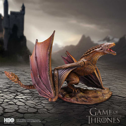 Dragon figurine from 'Game of Thrones' on a textured surface with a castle silhouette in the background.