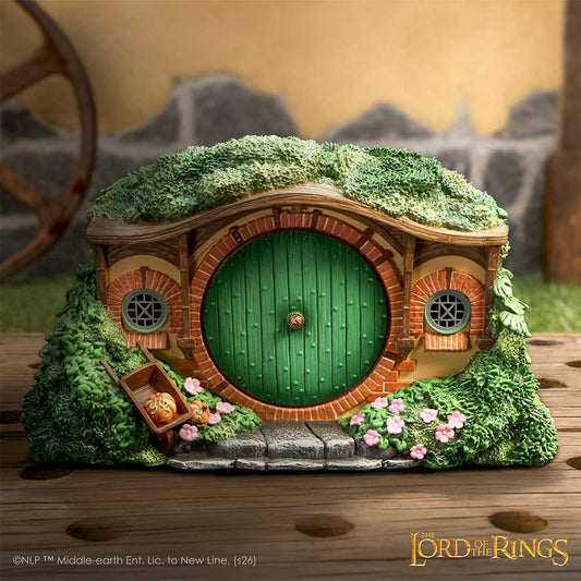 Model of a hobbit house with green door and mossy roof, inspired by 'The Lord of the Rings'.