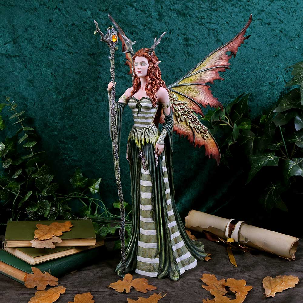 Fantasy fairy figurine with wings and a staff, surrounded by books and leaves on a dark background